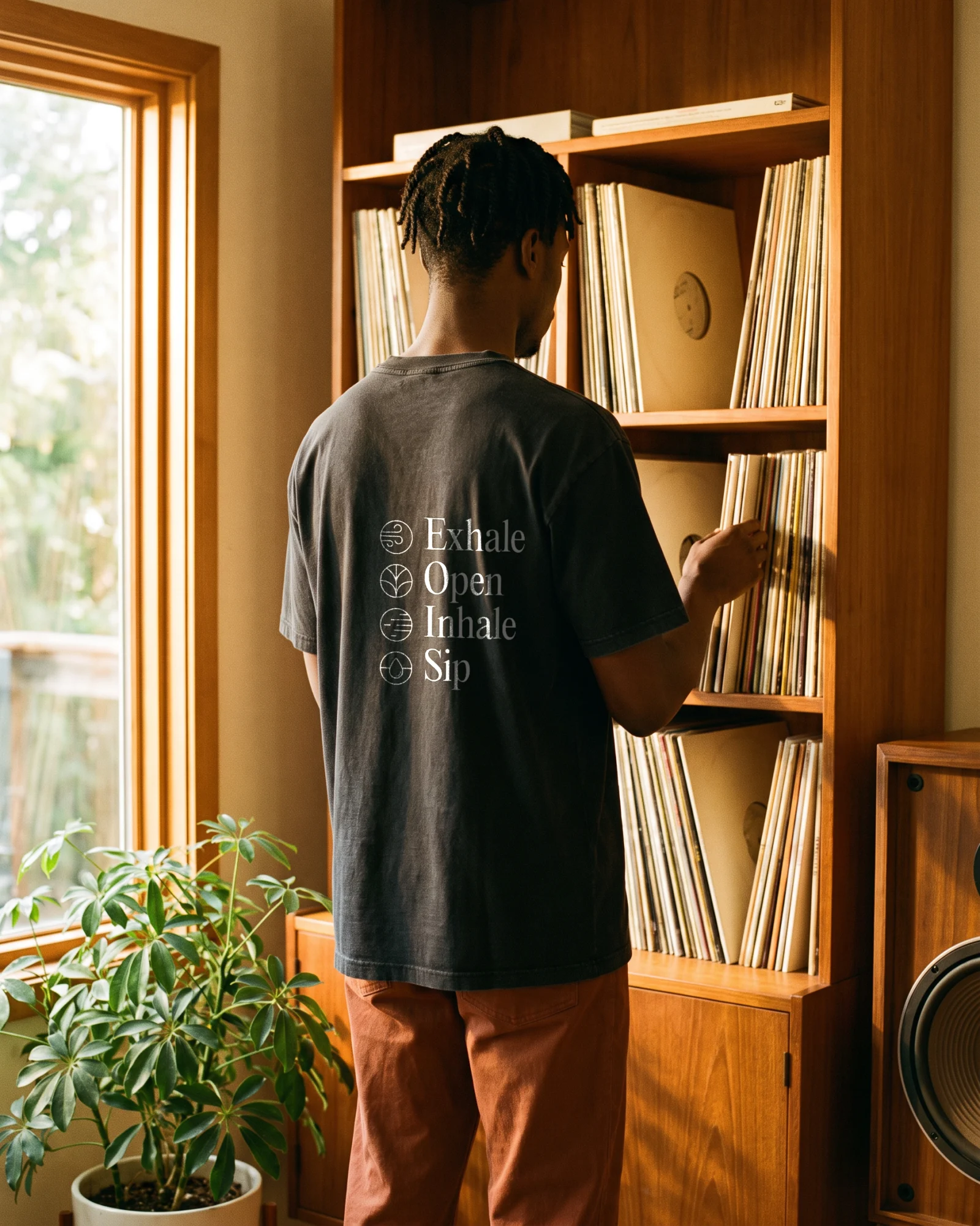 A man seen from behind at a shelf of records, wearing a washed black t-shirt with the four ritual words printed on the back