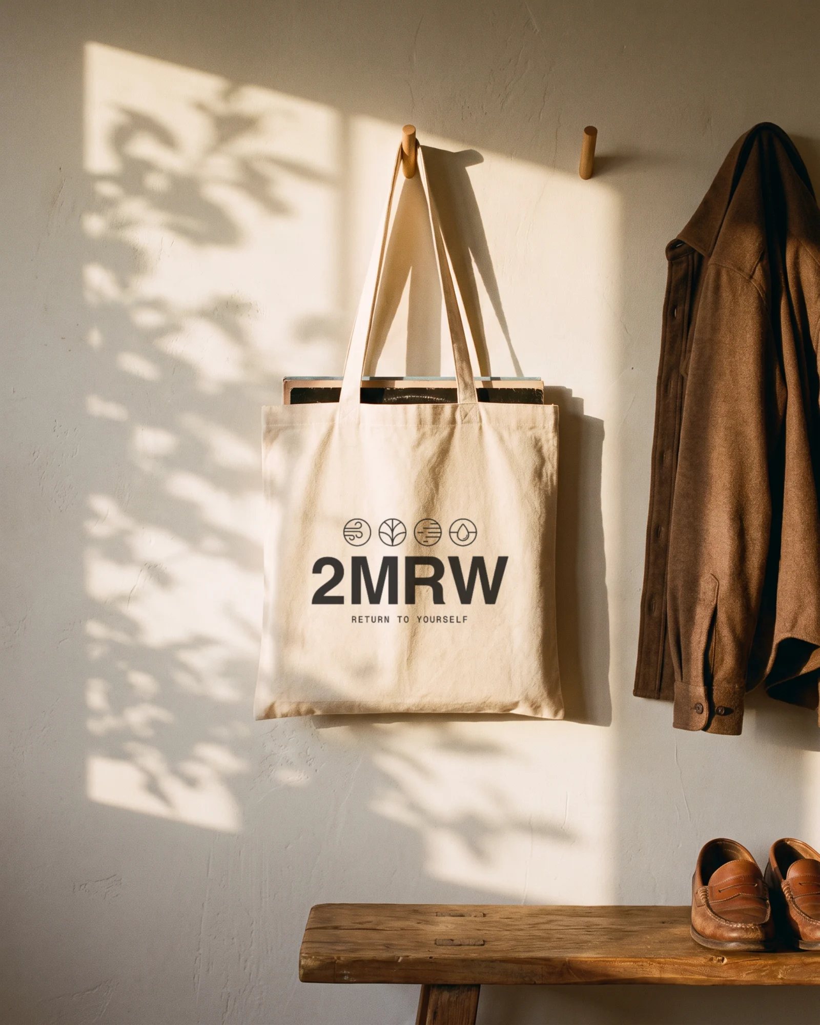 A cream 2MRW tote bag with records in it, hanging from a wall hook in afternoon sun
