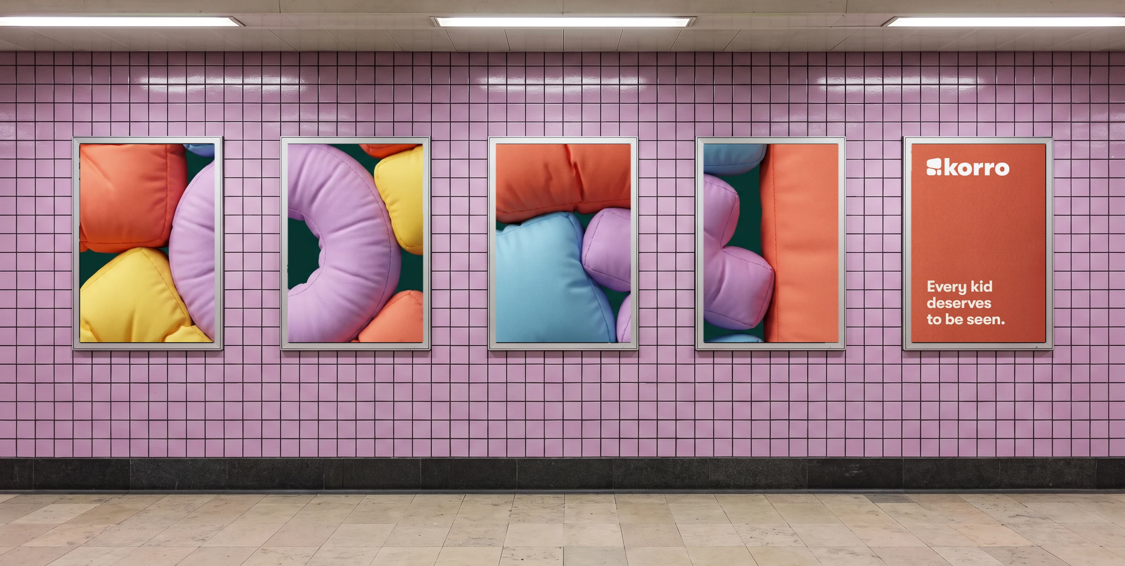 A metro platform with lilac tiles and five poster frames in a row; orange, blue, yellow and lilac cushions run across the first four, and the last is orange with the Korro logo and the line every kid deserves to be seen