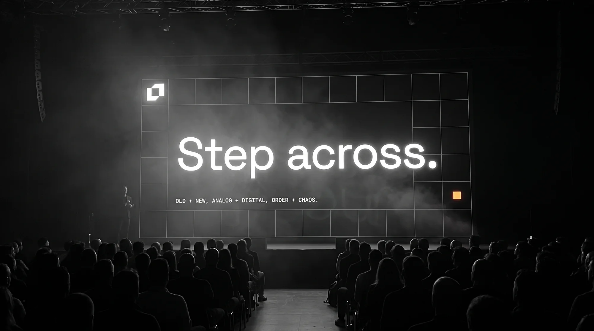A stage screen showing Step across. in front of a seated audience