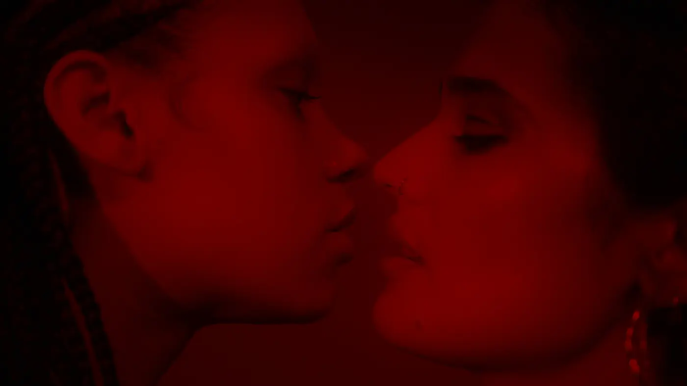 Two women in profile, lips almost meeting, lit red against black