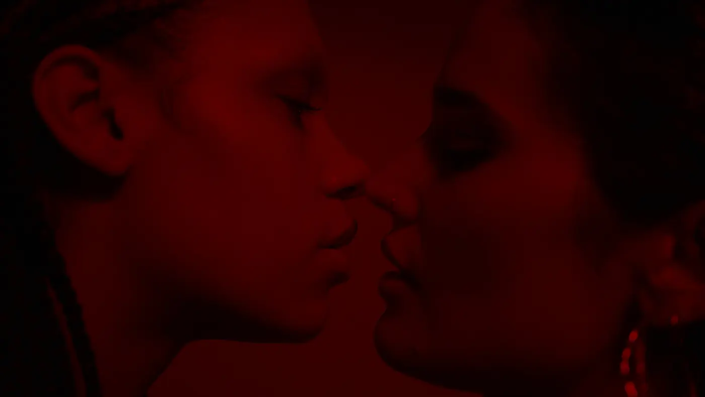 Two faces in profile almost kissing, noses touching, lit deep red against black