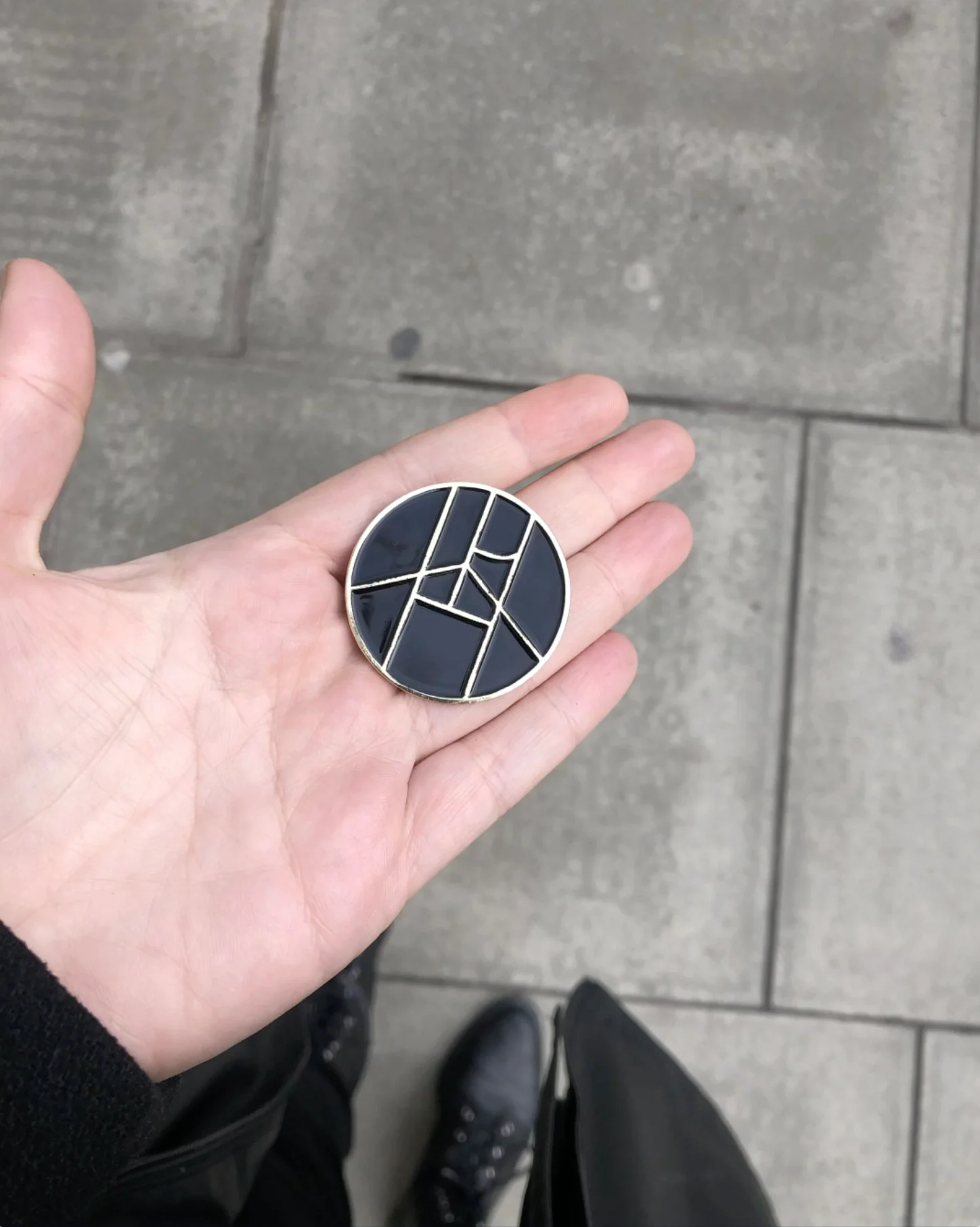 A hand holding the Playhouse symbol as a round enamel pin