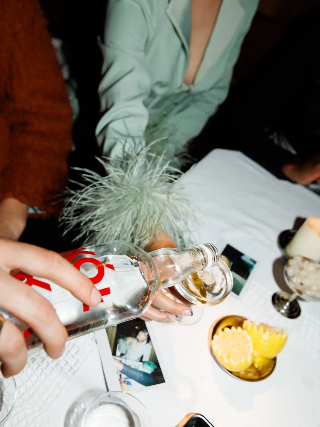 A hand pouring Sok&oacute;ł into a coupe over a table of lemons, photographs and cut crystal